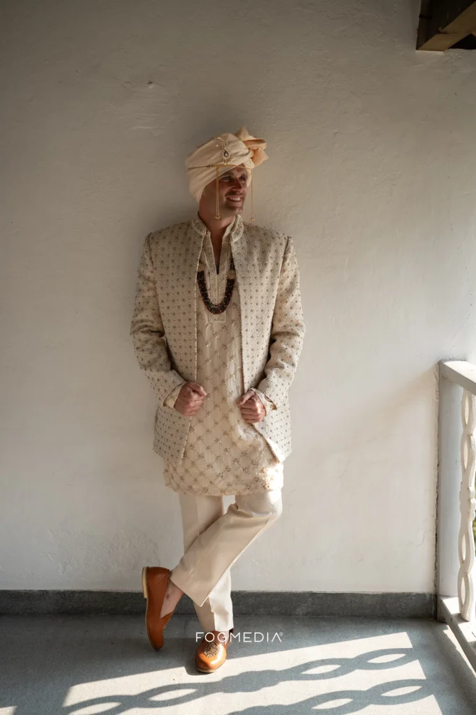 Full length portrait of David in his wedding sherwani against a white wall at Prainha
