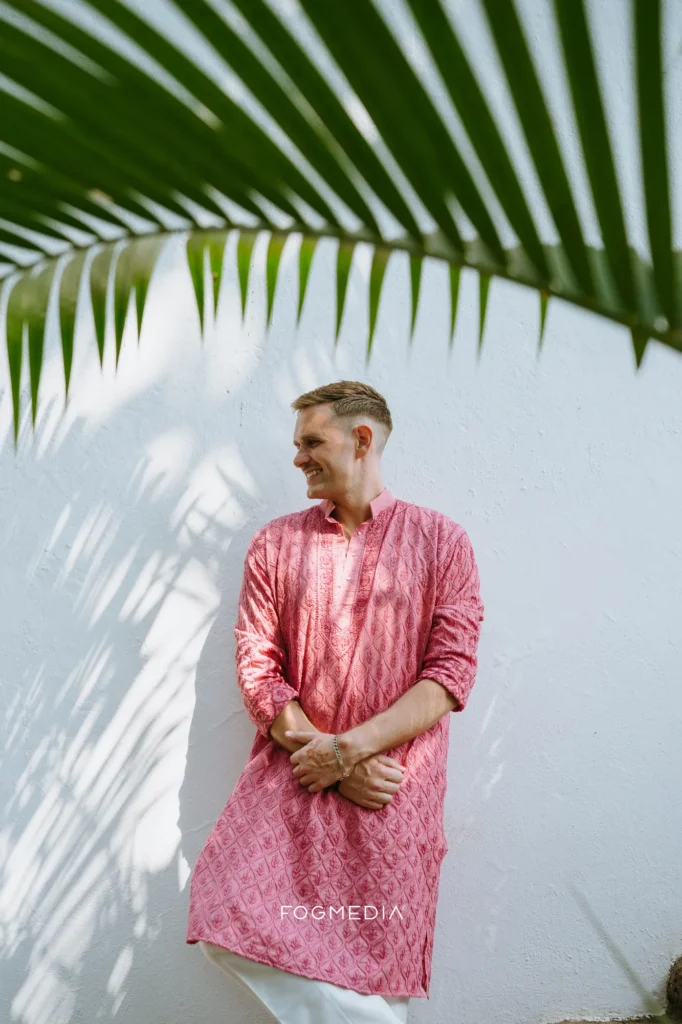 David in a pink kurta against a white wall at Prainha, palm shadow across the frame
