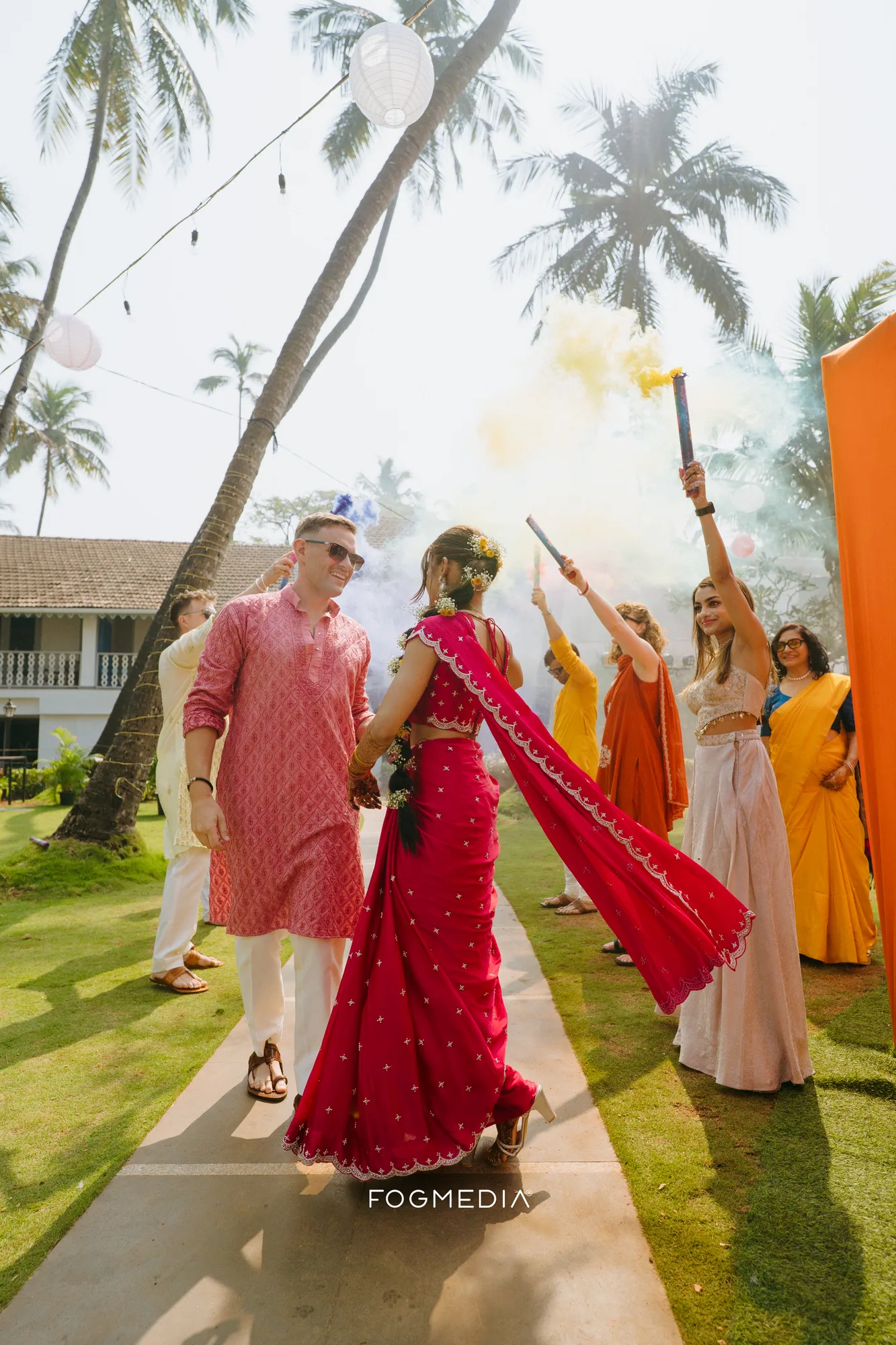 Salonee and David walking into their haldi at Prainha under smoke flares, guests in yellow behind them