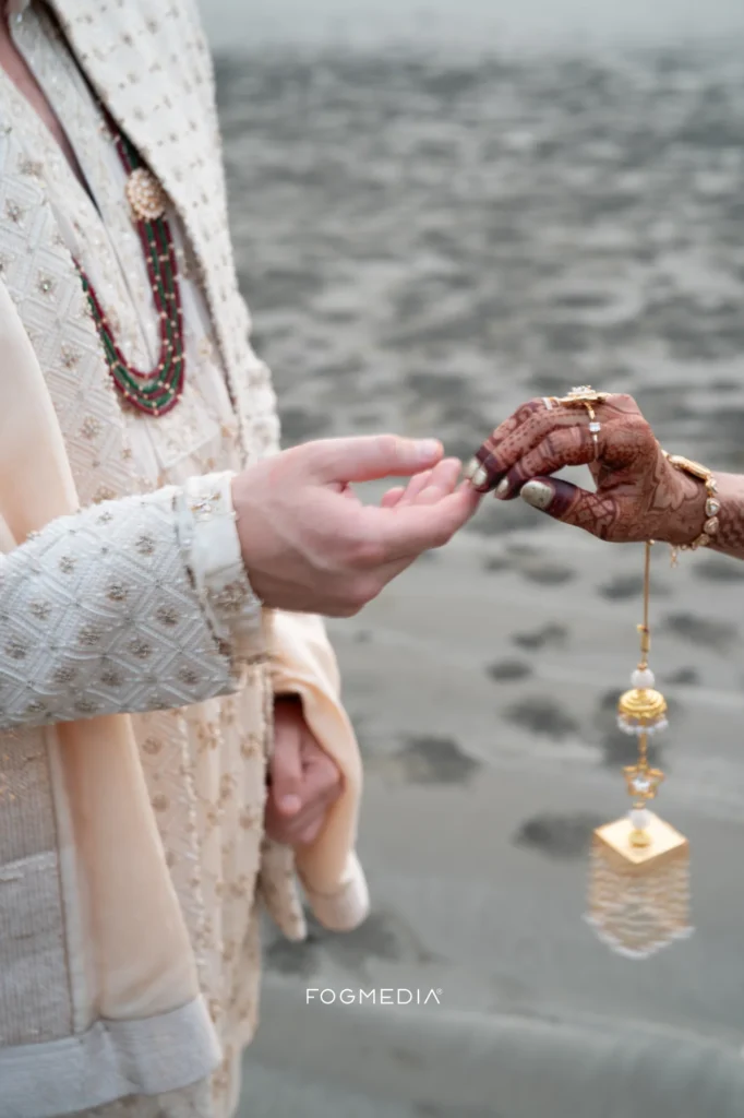 David holding Salonee's mangalsutra on the beach, her hennaed hand and wedding ring in frame