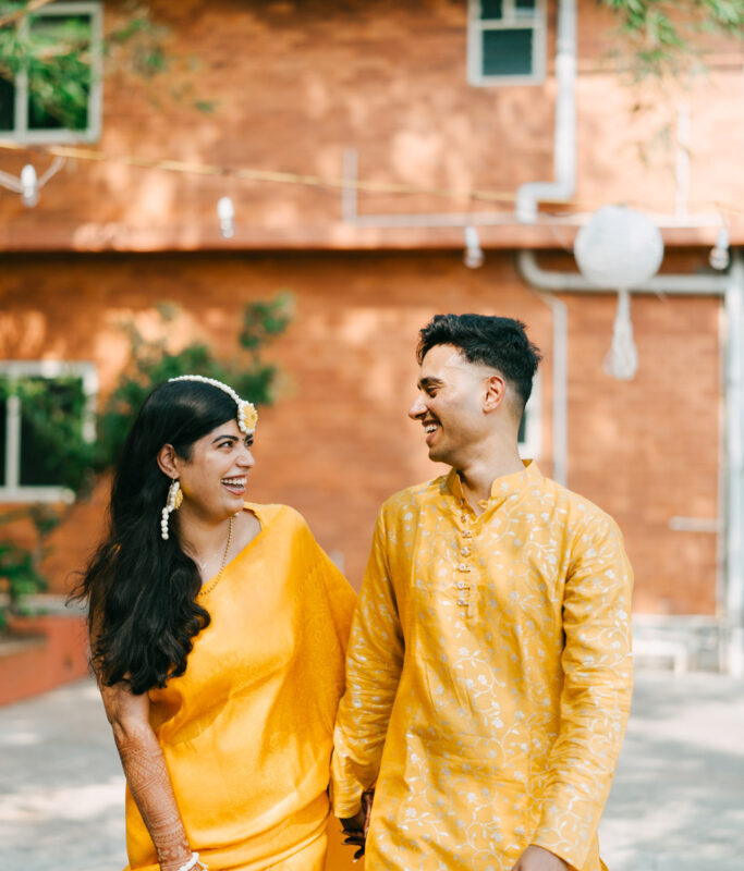 A Fog Media photographer framing a shot on a film camera while a couple in cream Kerala wedding dress laugh in the foreground